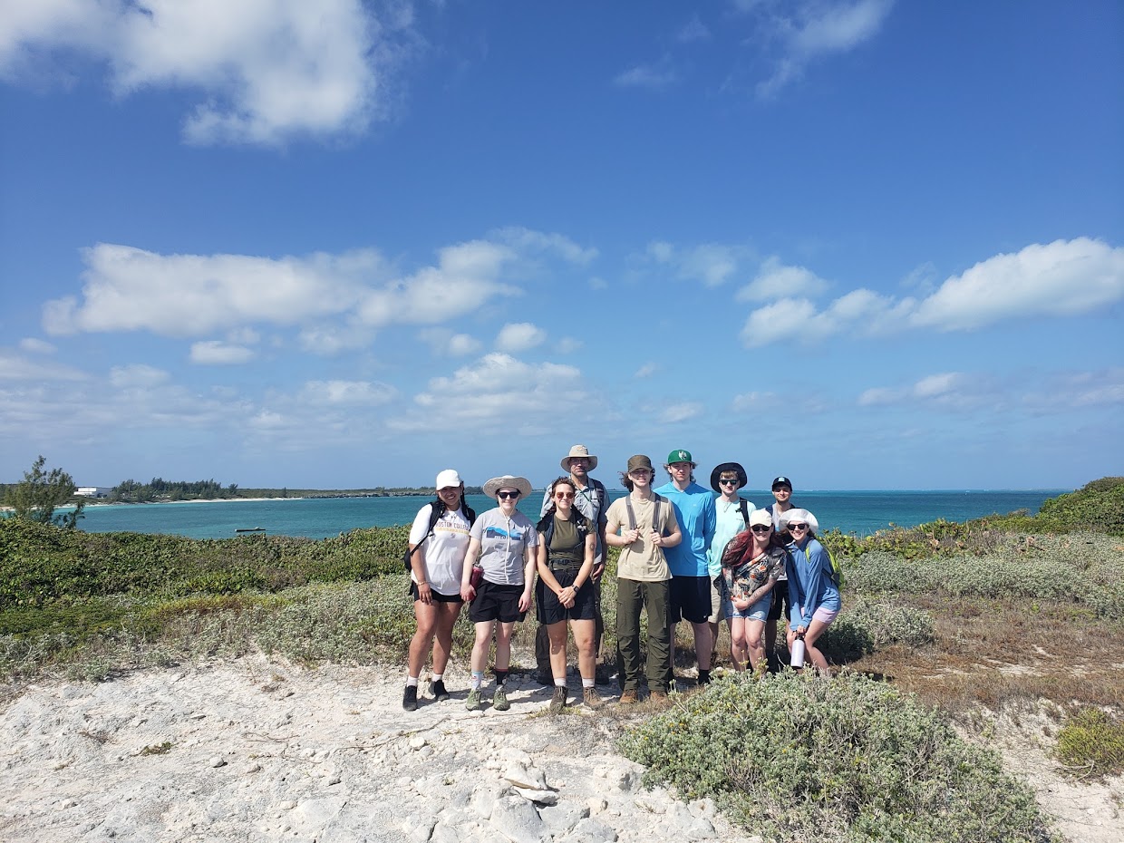 students stand on the beach in front of the ocean during a travel course. 