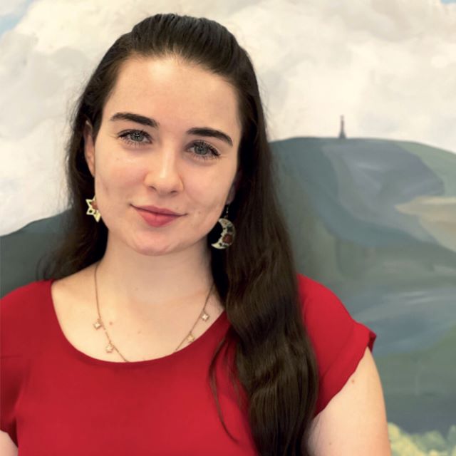Jordan, wearing earings and a necklace with a mural of mount greylock behind them